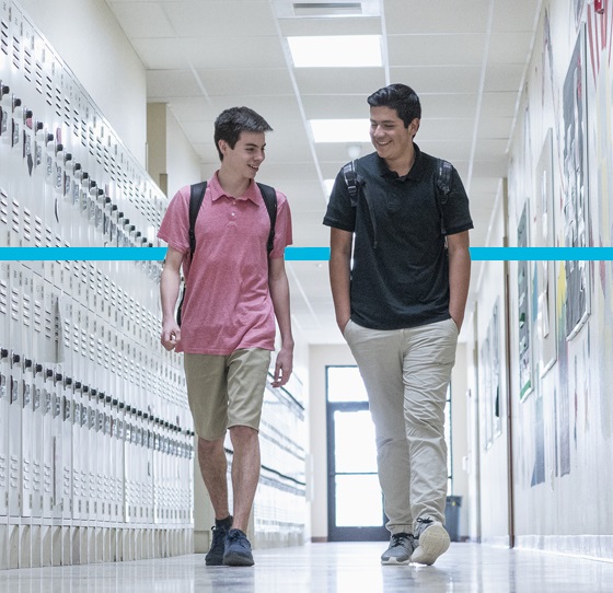 Two high school students walking by lockers.